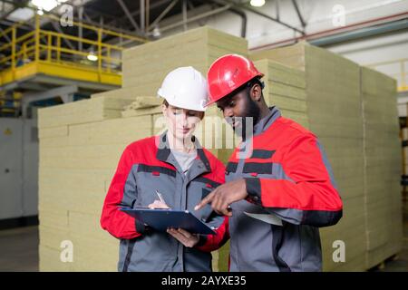 Horizontal medium portrait of male and female construction supplies factory workers making report together Stock Photo