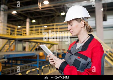 Horizontal portrait shot of professional female factory worker wearing uniform using tablet PC Stock Photo