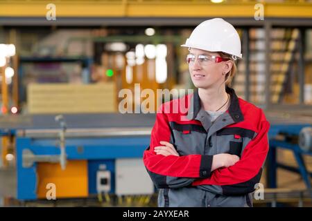 Horizontal medium portrait of attractive Caucasian female factory engineer standing with arms crossed looking away smiling Stock Photo