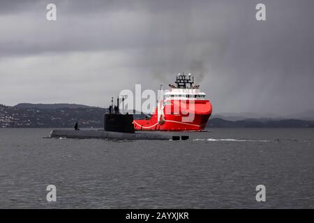 Norwegian submarine KNM Uredd S305 of the Ula class, departing from port of Bergen, Norway. In background, offshore AHTS Anchor Handling Tug Supply ve Stock Photo