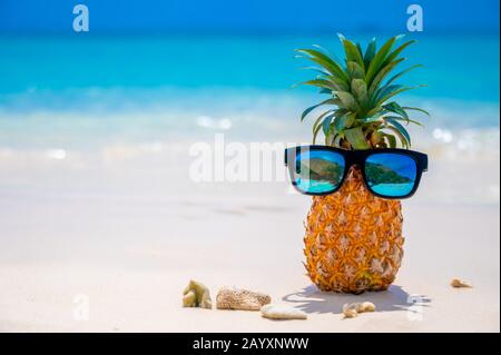 Glasses pineapples are located on the beach by the sea in the hot sun, setting the concept for summer. Stock Photo