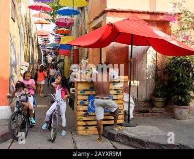 Street art and overhead umbrellas provide color and shade on Callejon Angosto in Getsemani, Cartagena, Colombia Stock Photo