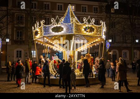 Warsaw, Poland - December 27, 2019: People with children having fun at carousel roundabout amusement ride at night during Christmas holiday season on Stock Photo