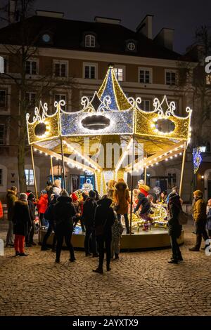 Warsaw, Poland - December 27, 2019: People with children having fun at carousel roundabout amusement ride at night during Christmas holiday season on Stock Photo