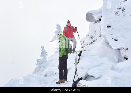 two male travelers in the winter mountains among the snowy cliffs during a blizzard Stock Photo