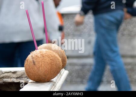 Two coconuts left on marble in the middle of the street. There are colored straws on it. Stock Photo