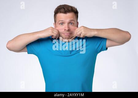Problems with skin. Caucasian man in blue t-shirt stretching his skin on face. Studio shot Stock Photo