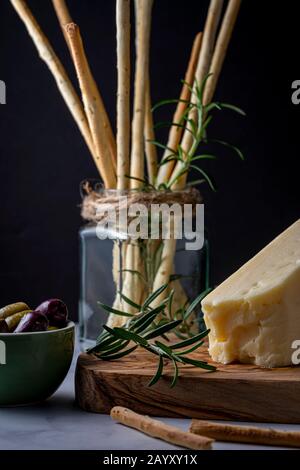 Grissini snack bread sticks and Asiago cheese with olives. Stock Photo