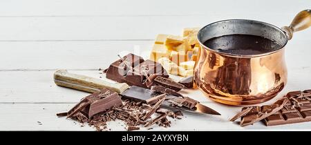 Preparing a chocolate sauce or dip with chopped and flaked assorted bars alongside a copper pot with melted chocolate in a banner format over white wo Stock Photo