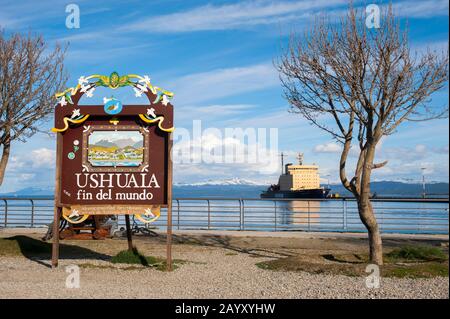 The end of the world sign in Ushuaia, the capital of Tierra del Fuego in Argentina, with the Beagle Channel and the Russian icebreaker Kapitan Khlebni Stock Photo