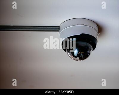 Dome surveillance camera in a transparent hemisphere. CCTV video camera on the white ceiling in the subway Stock Photo