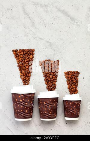 Coffee beans opposite three paper cups of different coffee capacities, vertical image. Stock Photo