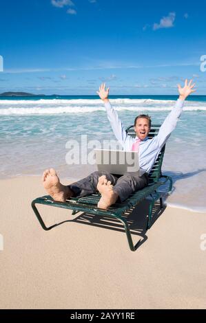 Excited barefoot businessman celebrating outdoors with his computer on a tropical beach Stock Photo