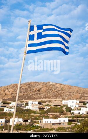 Greek flag waving from a long flagpole in sunny blue Mediterranean sky on the rocky island of Mykonos, Greece Stock Photo