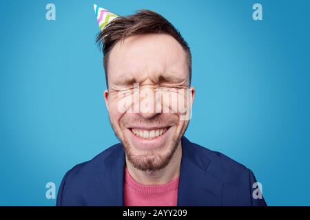 Portrait of distraught young man in jacket sitting at table and screaming through magnifying glass against blue background Stock Photo