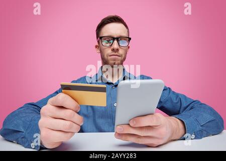 Portrait of serious intelligent young bearded card player in glasses sitting at table and throwing cards to camera Stock Photo