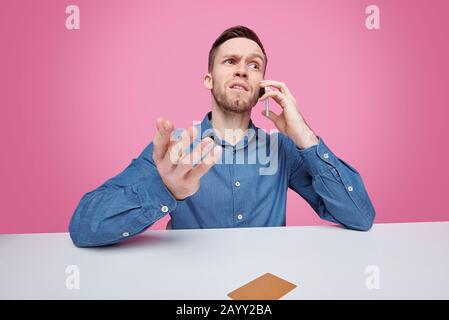 Serious young man in jacket sitting at table and solving cube puzzle while developing logic Stock Photo