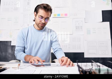 Young man wearing eyeglasses sitting at office desk using modern tablet PC, horizontal shot Stock Photo