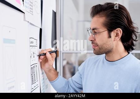 Horizontal side view chest up portrait of young male application developer making notes on scheme Stock Photo