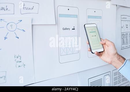 Unrecognizable IT specialist comparing new software sketch on his smarphone screen with one on paper Stock Photo