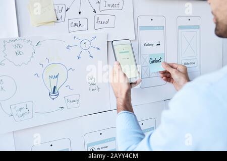 Horizontal shot of unrecognizable young man in light blue sweater working on smartphone application design Stock Photo