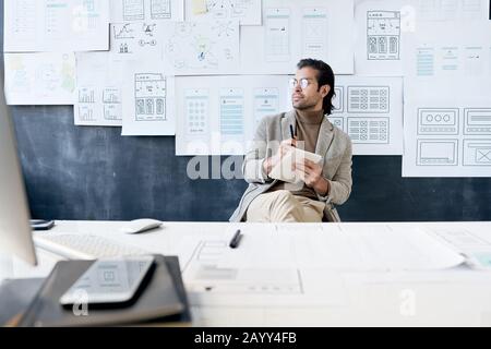 Horizontal shot of Caucasian man working on something making notes in his notebook looking away Stock Photo