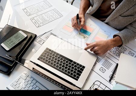 Unrecognizable professional software designer sitting at desk working on new mobile application sketch, horizontal high angle shot Stock Photo
