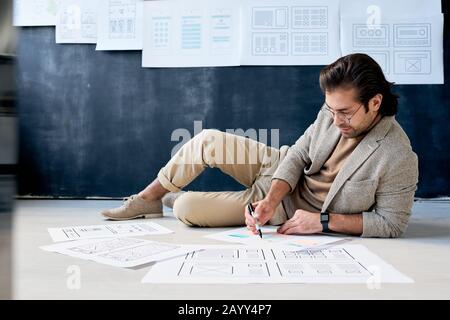 Horizontal shot of modern application designer doing his job relaxing on floor in office room Stock Photo