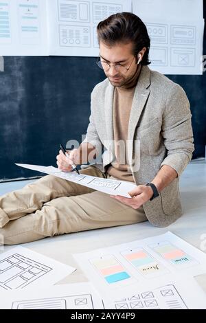 Vertical portrait shot of modern application designer doing his job sitting on floor in office room Stock Photo