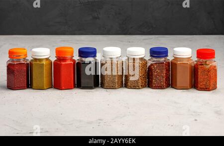 Various seasonings in glass transparent jars on a gray concrete background. Stock Photo
