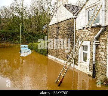 NANTGARW, NEAR CARDIFF, WALES - FEBRUARY 2020: Ladder against house and a car submerged in  floodwater on a road after the River Taff burst its banks Stock Photo
