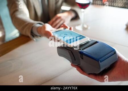 Horizontal high angle close up shot of unrecognizable man paying for meal in restaurant using NFC on smartphone Stock Photo
