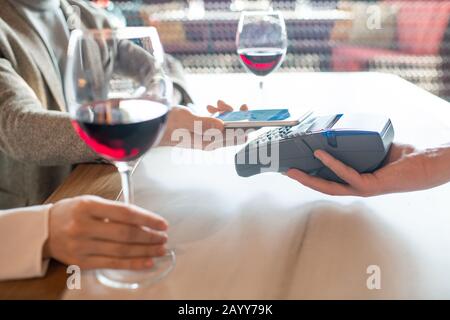 Horizontal shot of unrecognizable person paying for meal order in modern cafe using NFC on smartphone Stock Photo