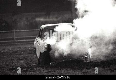 1970s, historical, a banger racing car with smoke pouring out from a battered engine, England, UK. In banger racing, old scrap cars are used and contact to crash into and damage opponents cars is allowed resulting in smashed up cars stuck on the circuit. Stock Photo