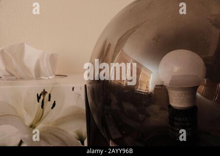 See-through glass dome table lamp (upside down fishbowl?) showing reflected blinds and the bulb inside. Box of tissues behind. Stock Photo