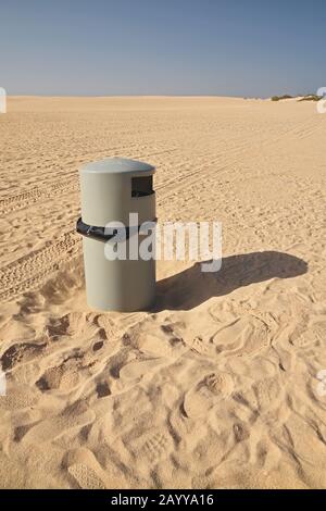 Single grey rubbish trash bin on beach on sunny day with blue sky Stock Photo