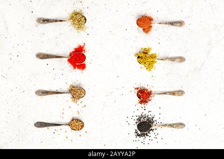 Various seasonings in old silver spoons on a background of gray concrete. Stock Photo