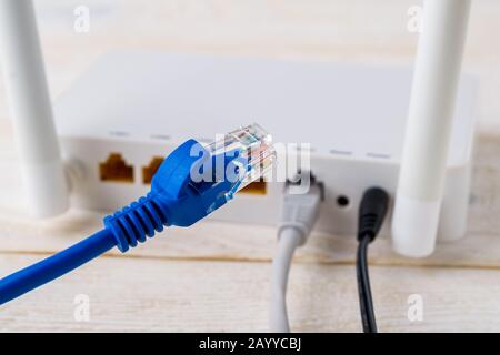 Close-up of blue network cable on a background of a white Wi-Fi wireless router on a white wooden table. Wlan router with internet cables plugged in. Stock Photo