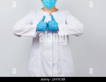 medic woman in white coat and mask, wearing blue medical latex gloves on her hands, showing like gesture in hand, approval concept Stock Photo