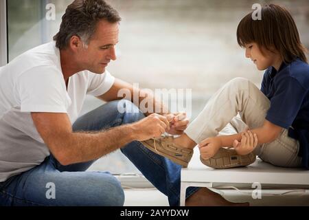 Middle-Aged man helps his young son to tie his shoelaces. Stock Photo