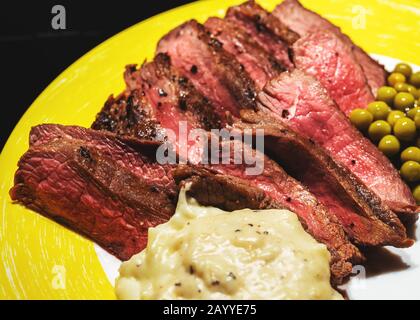 Medium-rare homemade steak with peas and cream sauce on yellow plate closeup isolated on black Stock Photo