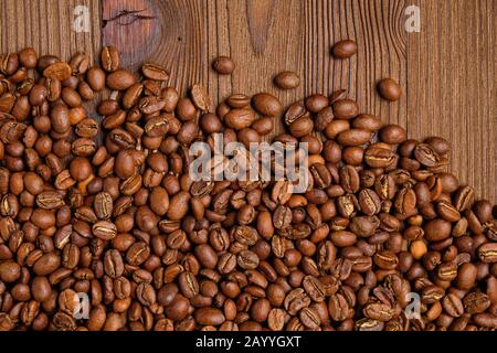 Scattered coffee beans on a burnt wooden background. Top view. Stock Photo