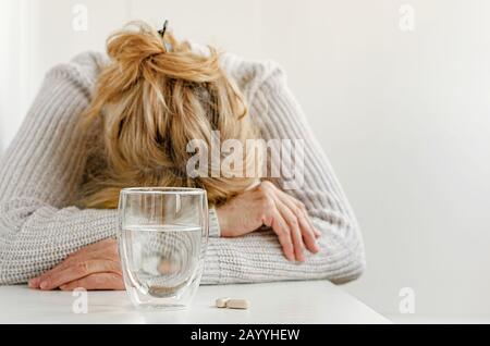 Elderly woman feeling stressed. Selective focus on glass and pills. Depression treatment concept Stock Photo