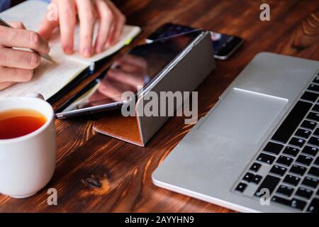 A man in a shirt makes notes in a diary and works on a laptop and tablet. Analytics activity concept. Close up. Stock Photo
