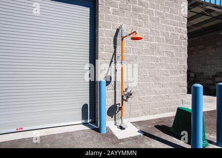 A free standing industrial safety shower with eye wash station stands outside a warehouse facility Stock Photo