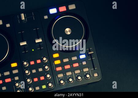 Dj sound mixer controller with knobs and sliders close up. audio mixing deck with turntables at dark with illuminated controls Stock Photo