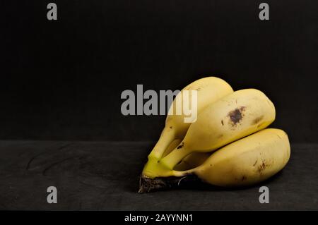 Some bananas seen on a table a black table and background with room for texts to the left of the image. Copy space and dark food style Stock Photo