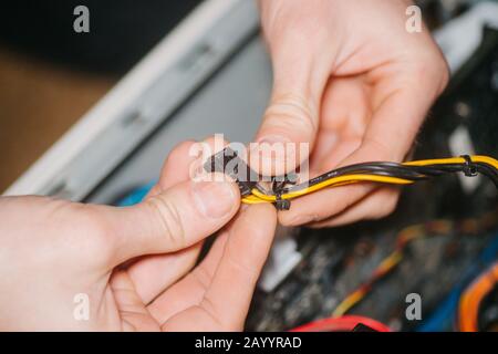 Professional system administrator holds in hands sockets connectors of standard power supply unit. man repairing and assembling computer. concept of d Stock Photo