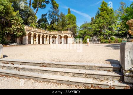 A solo female traveler walks through a gravel courtyard near an arched Roman building on Castle Hill in Nice, France. Stock Photo