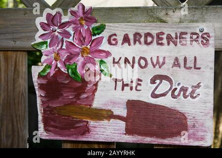 Close-up of a hand painted 'Gardener's know all the dirt' wooden sign in landscaped backyard garden in late spring. Stock Photo
